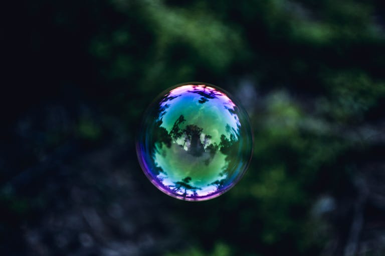 A colorful soap bubble reflecting trees and sky in a vibrant outdoor setting.